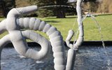 Section of an abstract silver fountain sculpture resembling intestines in a shallow pool stand with water squirting out the ends.