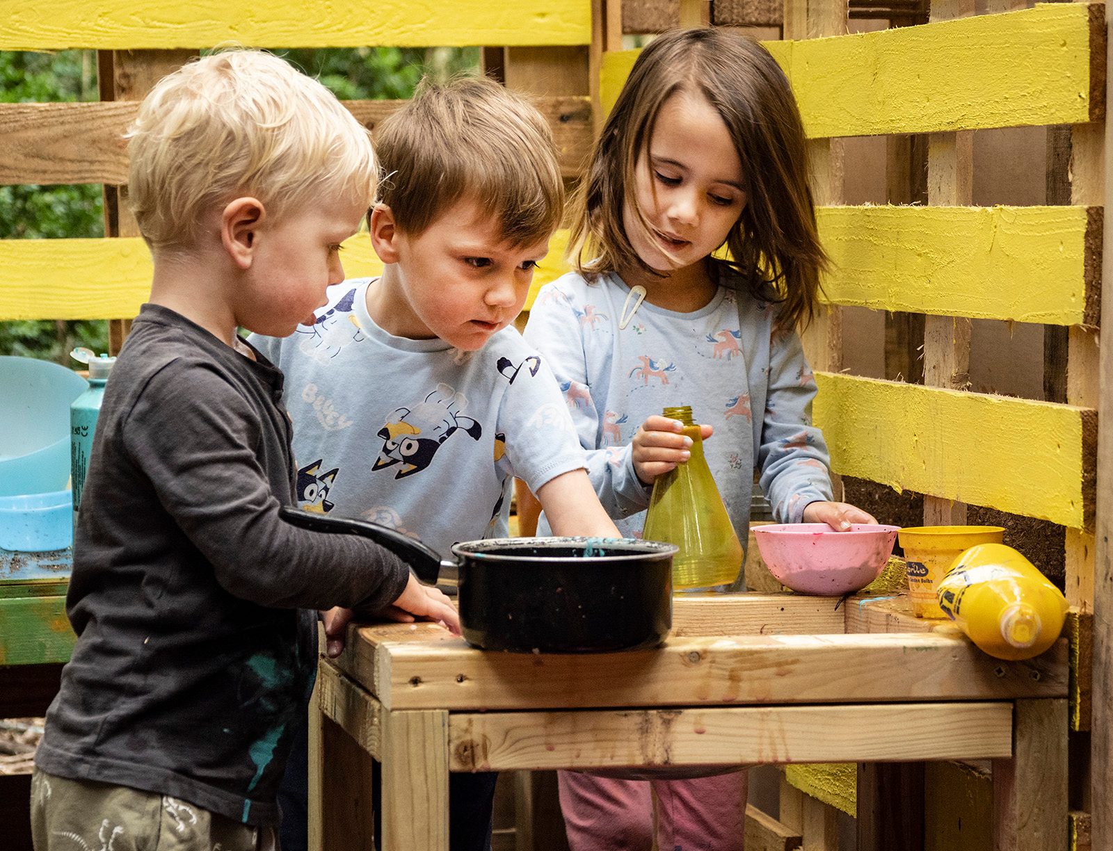 Three children outside playing with a mid kitchen with a yellow wooden background.
