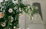 Green, pink and white wedding flowers cascade over a stone or marble tomb surrounded by classical architecture in what appears to be a chapel.