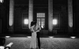 A bride and groom share a loving slow dance in the dark in front of a historical building with large classical columns and bright lights are shining out of the windows hinting at a lively reception going on inside.