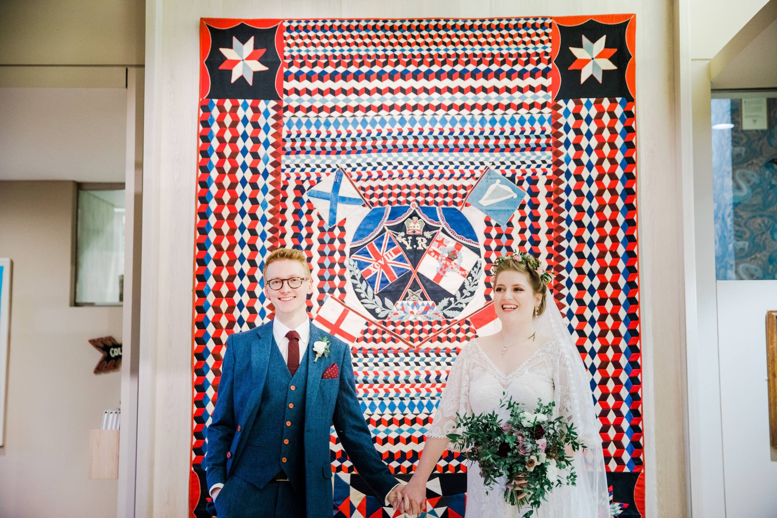 A bride and groom stand in front of a large red, white and blue military quilt