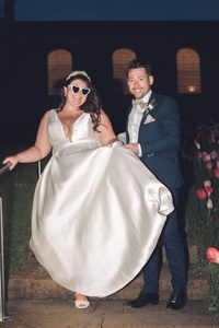 A bride in sunglasses in the dark walking down some stairs by a chapel