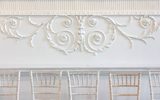 his image shows a white wall with classical motifs on it. It suggests a ballroom
