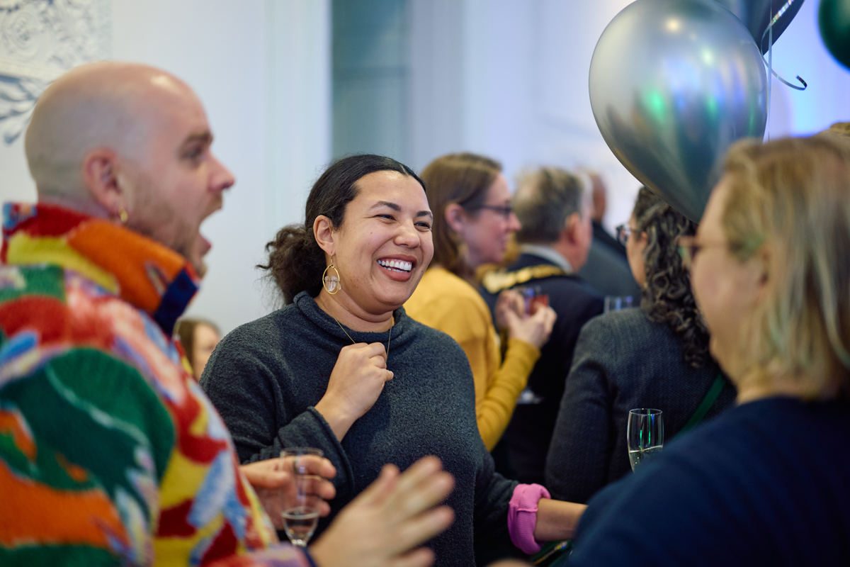 This image shows a group of people laughing in a gallery setting surrounded by balloons which indicates a celebration.