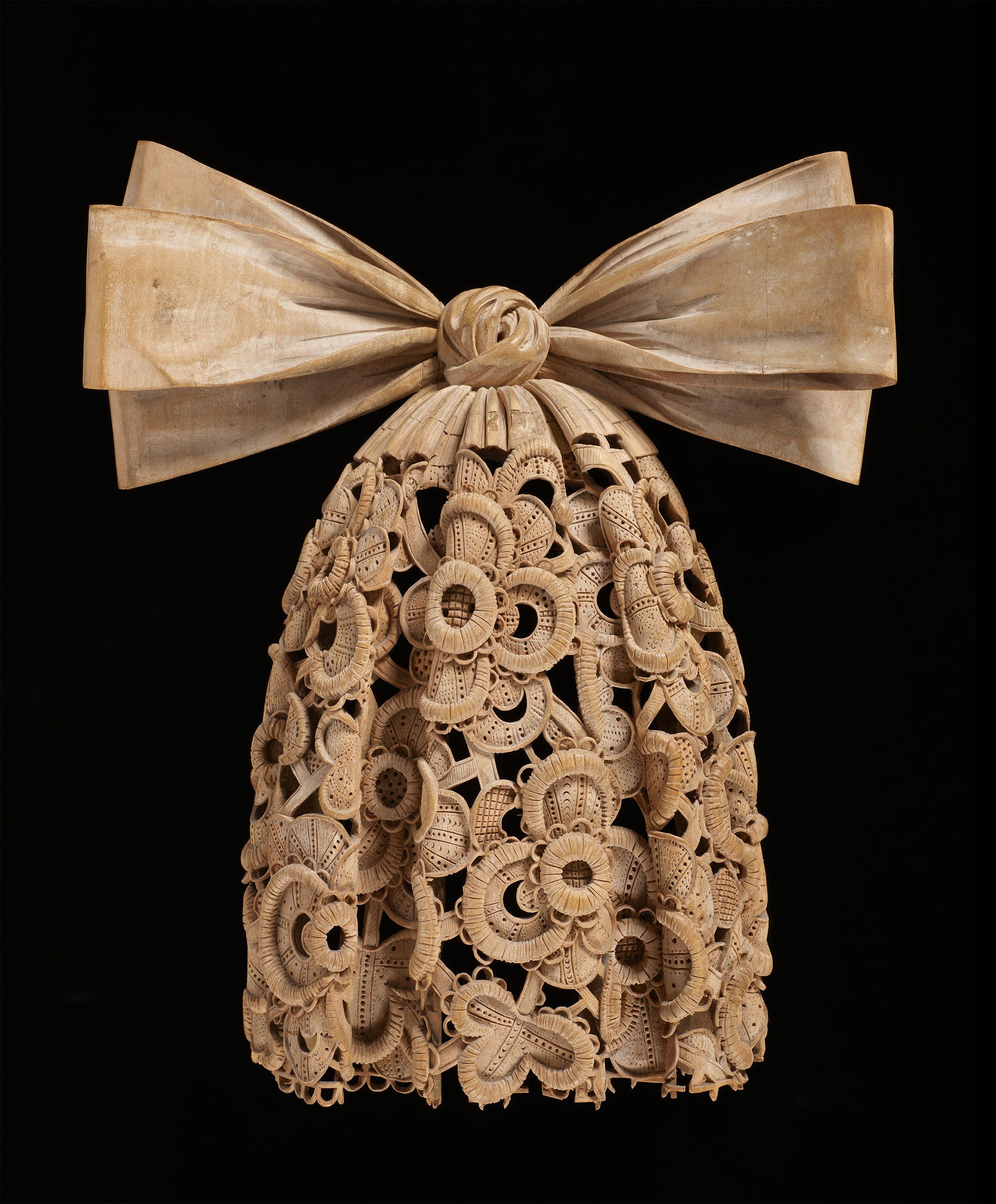 An intricately carved cravat, with a bow at the top and looks like lace, although it's carved from wood.