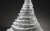 A sculptural stack of white, layered forms resembling a stylized Christmas tree against a black background.
