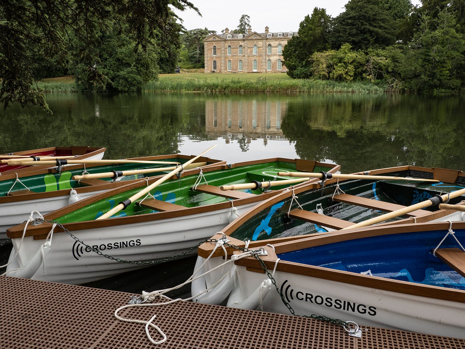 A stately manor house reflected in a tranquil lake, with a row of colorful rowboats in the foreground.