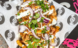 A tray of loaded fries with mean, red onion, herbs and sauce