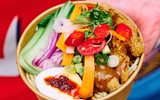 A bowl of Asian food including noodles, vegetables, egg and fried crispy chicken with sauce